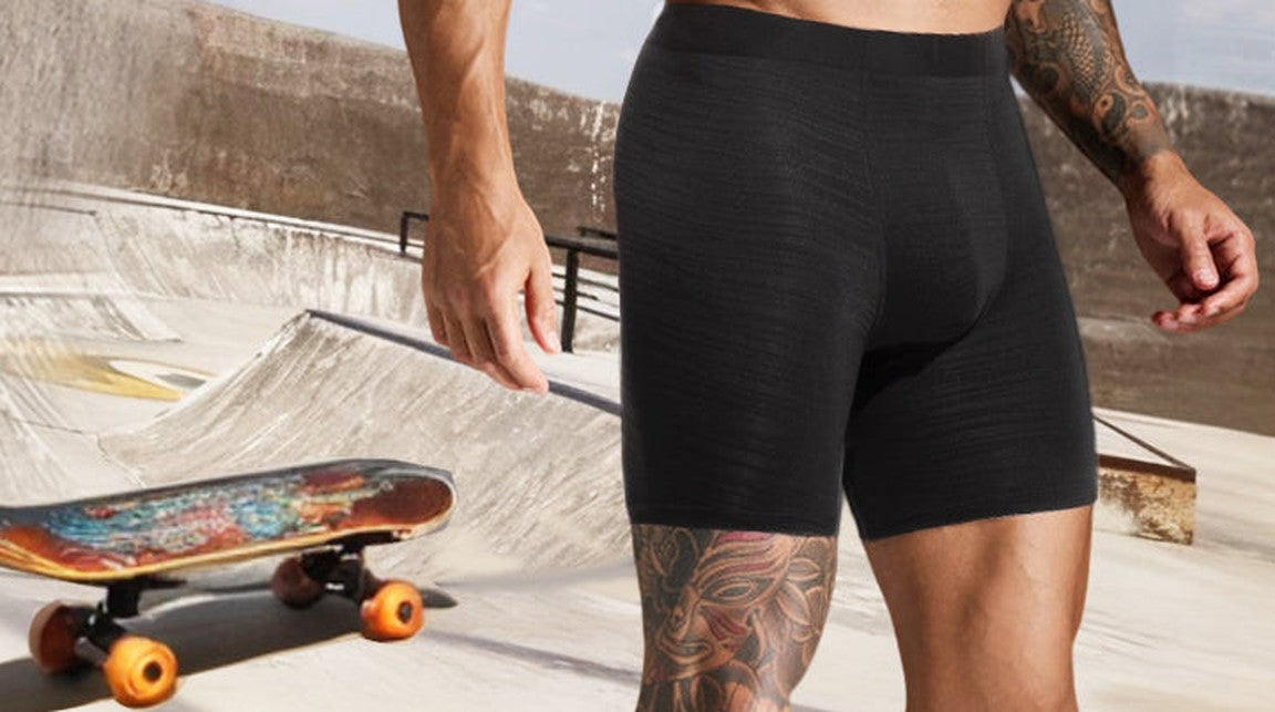 Man in black boxer briefs at a rooftop skate park next to a skateboard