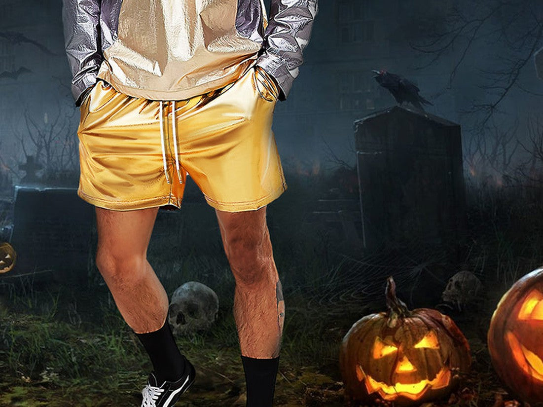 Man in gold metallic shorts, black socks and trainers next to carved pumpkins at night