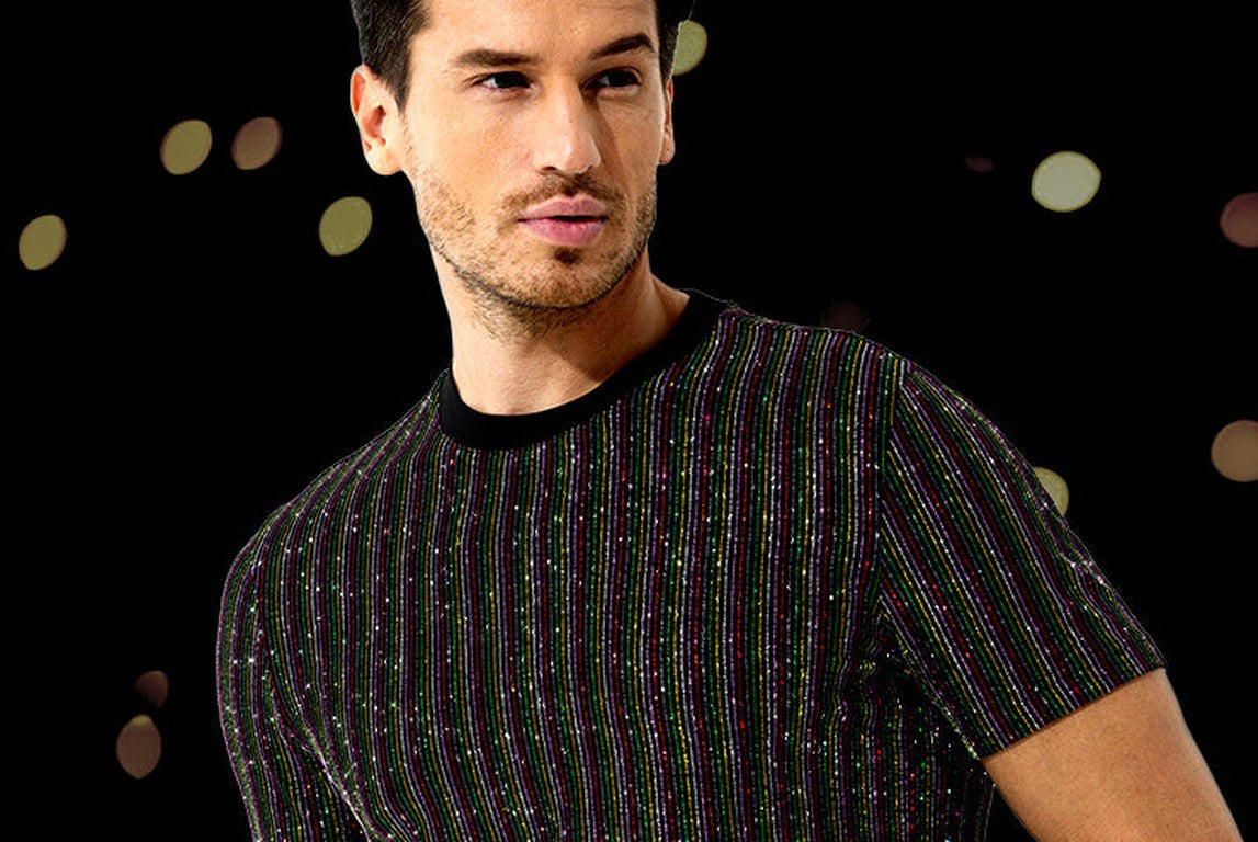 Man in a glitter striped party t-shirt against a dark background with festive bokeh lights