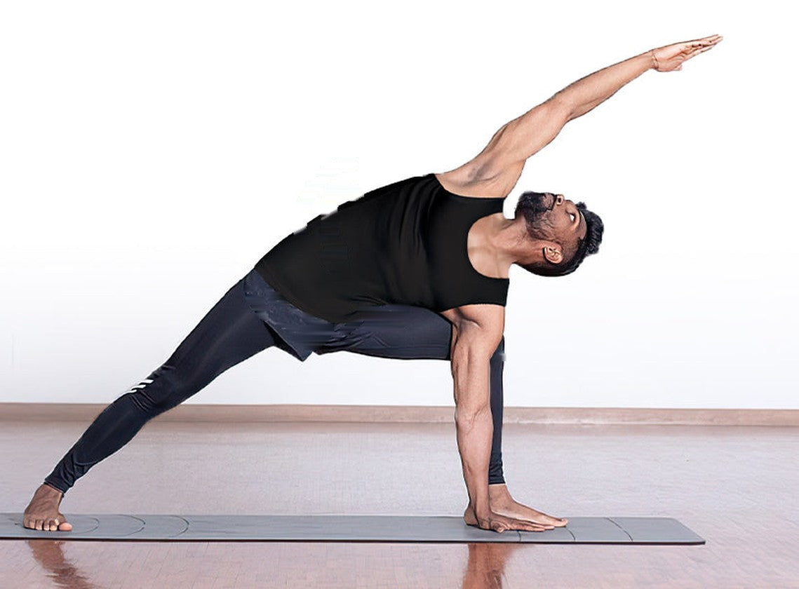 Man in a black compression tank top stretching on a yoga mat in a studio