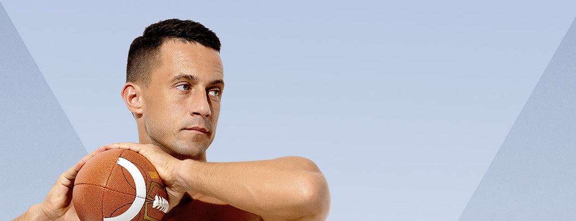 Athletic shirtless man holding a ball against a pale blue sky background