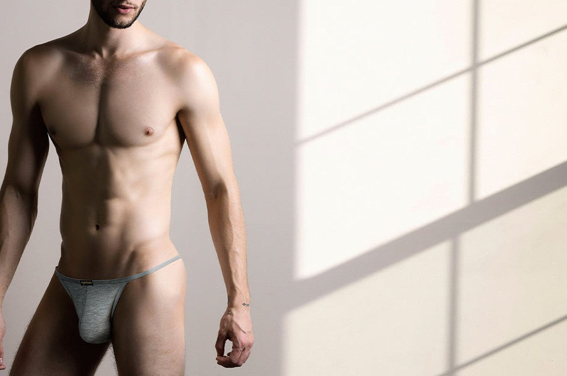 Man in grey Arjen Kroos low rise underwear standing against a sunlit wall