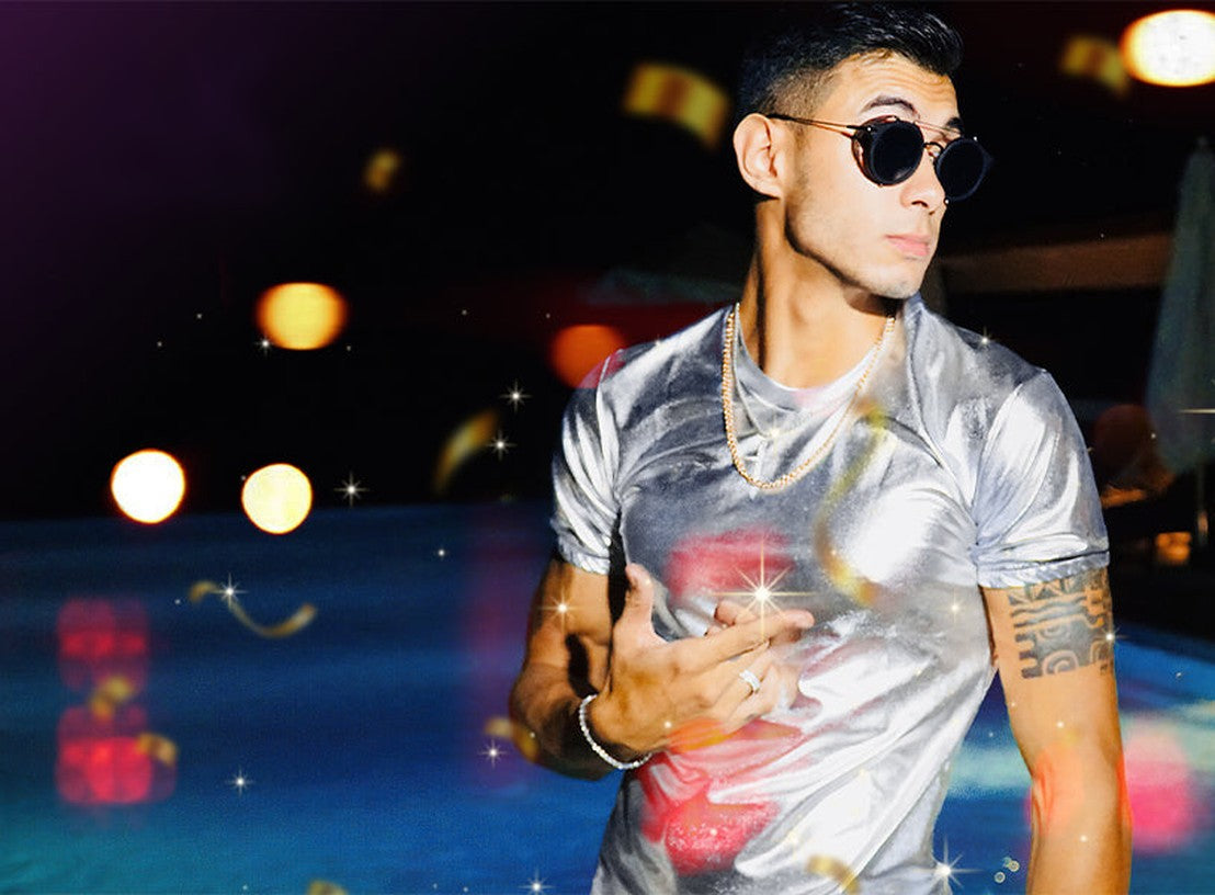 Man in a silver metallic t-shirt and sunglasses at a night-time pool party