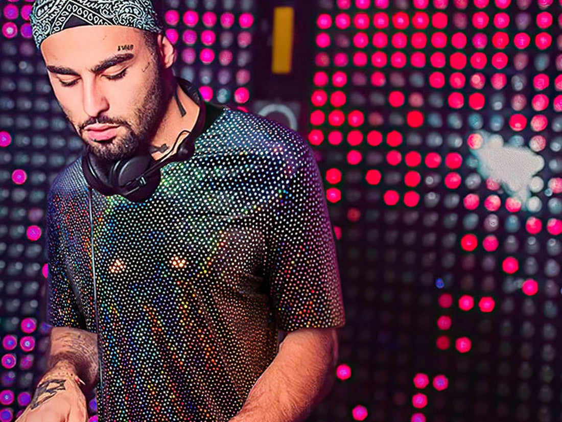 DJ wearing a sparkly holographic sequin shirt with headphones in front of a neon light wall