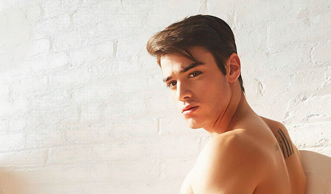 Man with dark hair looking over his shoulder against a white brick wall